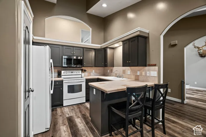 Kitchen featuring dark cabinetry, tile countertops, wood-finish flooring, high ceilings with decorative archways, and a built-in peninsula