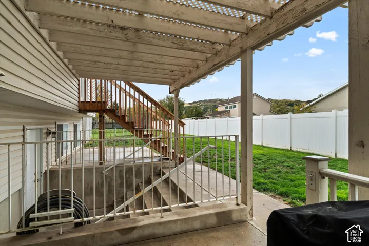 Covered patio featuring a timber pergola, concrete flooring, metal railing, and wood-finish exterior stairs