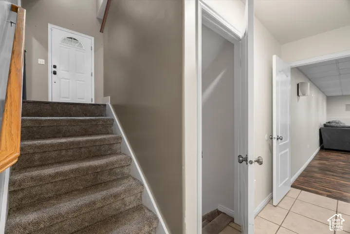 Entryway featuring carpeted stairs with a wooden handrail, white paneled doors, ceramic tile flooring, and wood-finish flooring