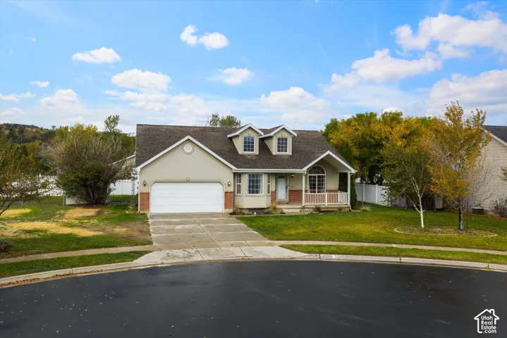 Split-level exterior featuring stucco and brick siding, a two-car garage, dual front dormers, and a covered porch