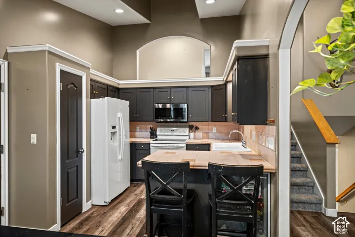 Kitchen featuring dark-toned cabinetry, a peninsula with tile countertop, vaulted ceilings, and wood-finish flooring