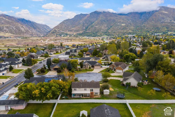Aerial perspective of a multi-level residential property featuring a rear covered patio, white vinyl perimeter fencing, and a detached storage structure, set against a prominent mountain backdrop