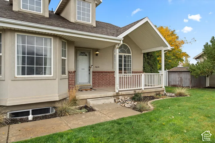 Stucco exterior featuring red brick accents, an arched window, a covered front porch with white railing, and dual dormer windows