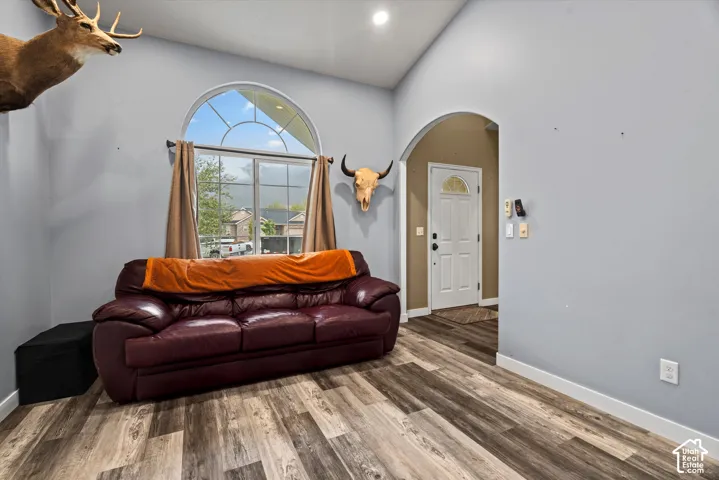 Vaulted ceiling room featuring wood-finish flooring, an arched window with muntin detailing, recessed lighting, and an arched doorway