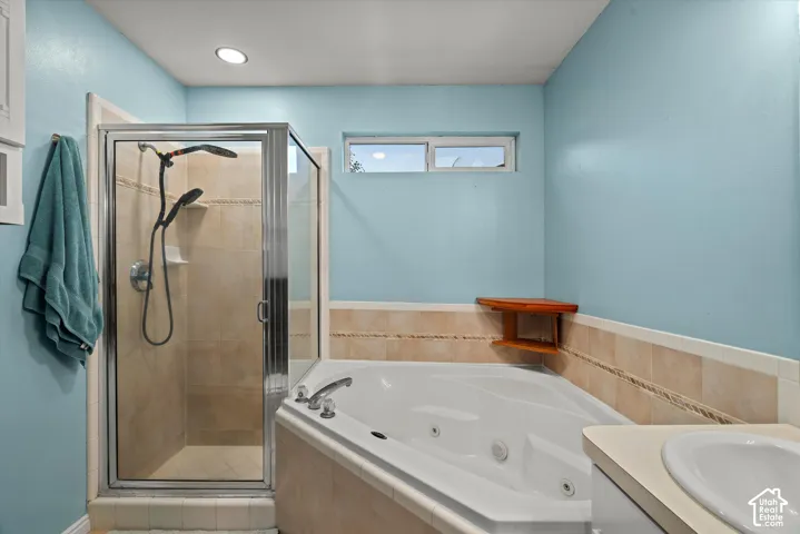 Corner jetted soaking tub and separate shower enclosure with neutral tile surround, complemented by a built-in wood corner shelf, recessed lighting, and a horizontal sliding window