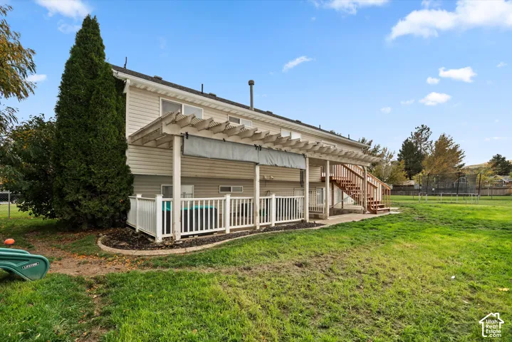 Rear exterior featuring a tiered pergola, elevated wood staircase, and an enclosed deck with a white railing