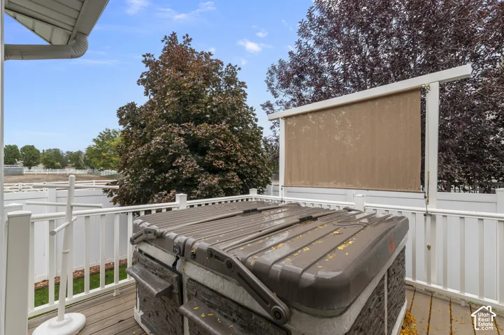Raised deck featuring a covered hot tub, privacy-screen frame, white picket-style railing, and perimeter vinyl fencing