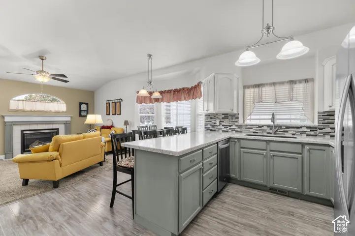 Kitchen featuring sage-toned cabinetry, light-toned stone-finish countertops, multi-toned horizontal tile backsplash, and stainless steel undermount sink, accented by a fireplace with a decorative mantel and arched top