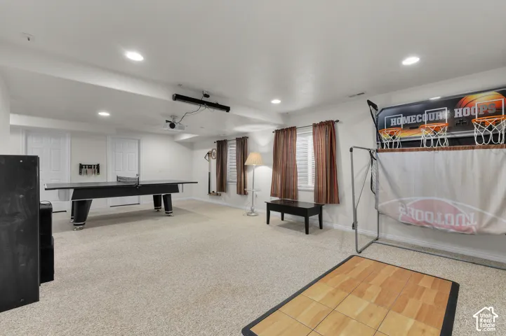 Spacious recreation area featuring neutral wall-to-wall carpeting, recessed ceiling lighting, and multiple windows with installed drapery