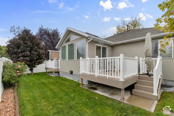 Rear exterior featuring a raised deck with white railings, a concrete patio foundation, stucco siding, and a fenced yard with mature landscaping