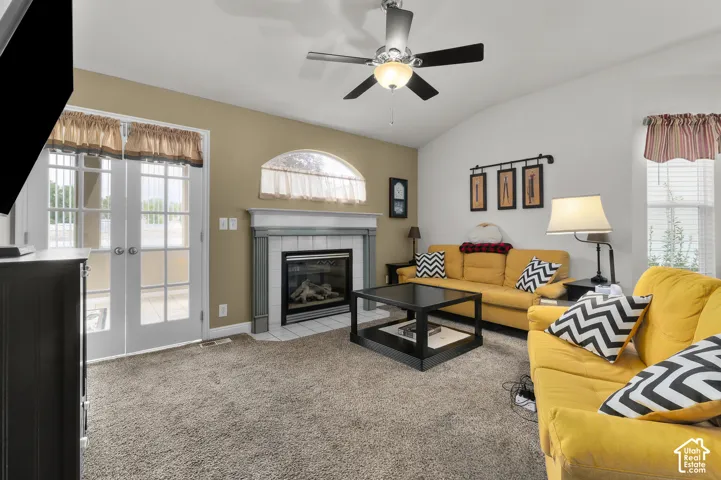 Living area featuring a fireplace with a light-toned tile surround, arched window, ceiling fan with integrated lighting, and full-glass panel French doors