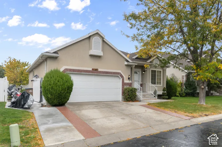 Stucco exterior with brick-accented garage surround, two-car garage, concrete driveway, and covered front entry