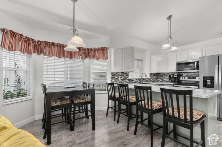 Kitchen featuring white cabinetry, stone-finish countertops, decorative tile backsplash, wood-finish flooring, and pendant lighting