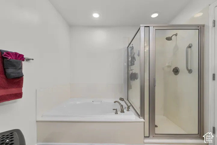 Built-in soaking tub with deck-mounted faucet and handheld shower attachment, enclosed glass shower stall with metallic trim, and recessed ceiling lighting