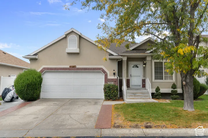 Stucco exterior featuring brick detailing, a concrete driveway, an attached garage, and a covered front entry with steps