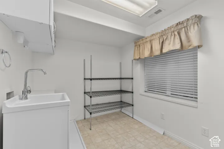 Utility area featuring a deep basin sink with a polished faucet, upper cabinetry, and horizontal window blinds