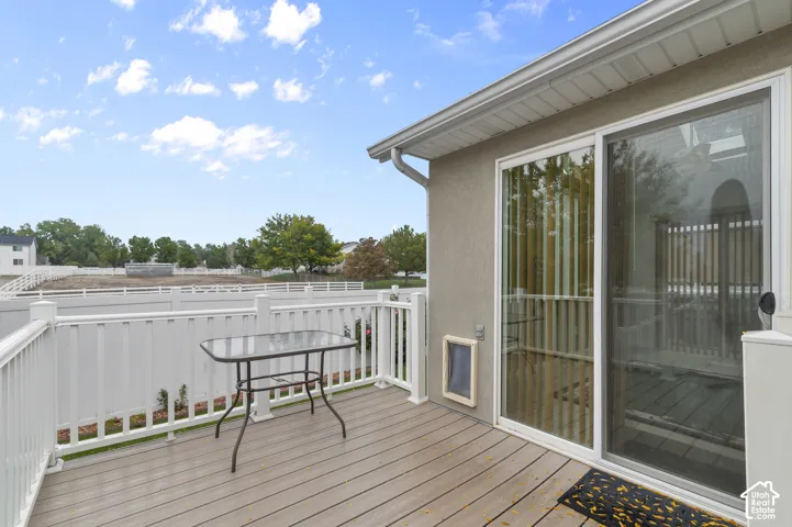 Elevated composite deck featuring white vinyl railings, sliding glass door entry, and stucco exterior siding