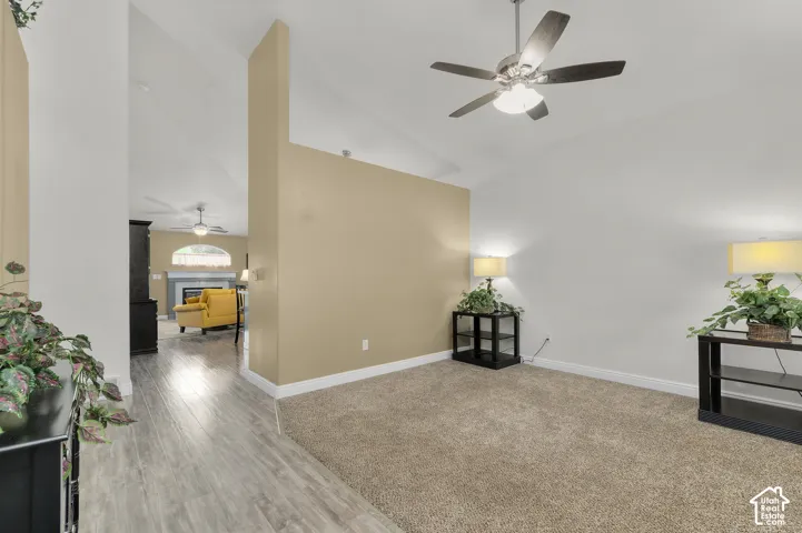 Vaulted ceilings, wood-finish flooring, neutral wall tones, and ceiling fan fixture