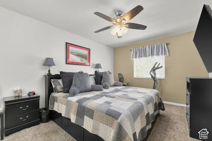 Neutral-toned bedroom featuring wall-to-wall carpeting, a multi-blade ceiling fan with integrated lighting, and a single-pane window with horizontal blinds