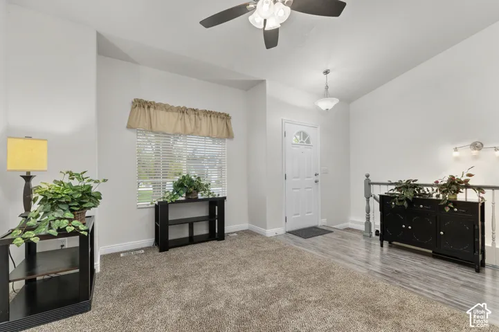 Entryway featuring vaulted ceilings, a ceiling fan with integrated lighting, wood-finish flooring, carpeted floor space, and a six-panel exterior door with a window insert