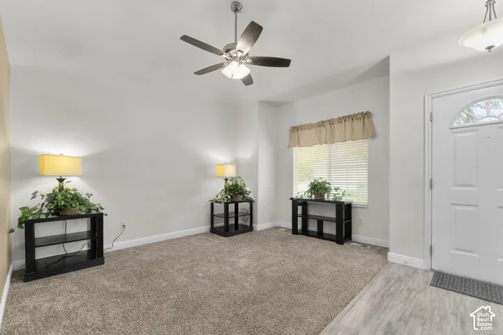 Neutral wall tones, ceiling fan with integrated lighting, wall-to-wall carpeting, wood-finish flooring at the entryway, and exterior door with a semi-circular transom window