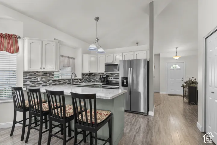 Kitchen featuring white cabinetry, stone-finish countertops, multi-toned tile backsplash, stainless steel appliances, and wood-finish flooring