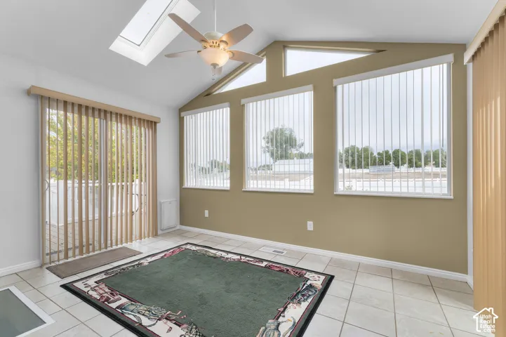 Vaulted ceiling featuring a skylight, ceiling fan, and large windows with vertical blinds, finished with tile flooring and a sliding glass door