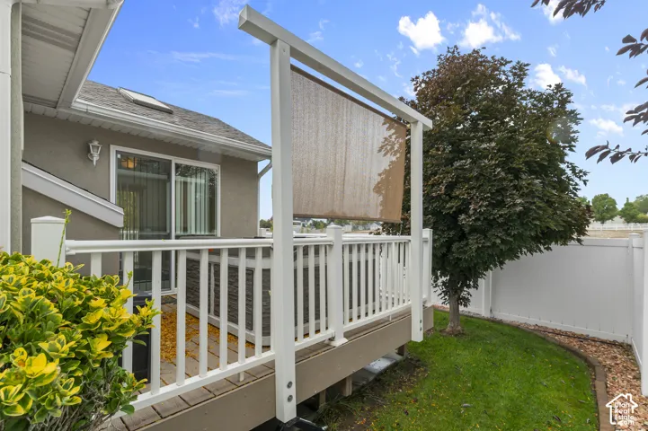 Elevated wood-tone deck featuring white vinyl railings, an adjustable privacy screen, an integrated spa, and an enclosed lawn with perimeter white fencing