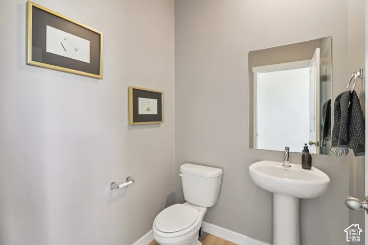 White pedestal sink with chrome faucet, frameless wall mirror, and wood-finish flooring