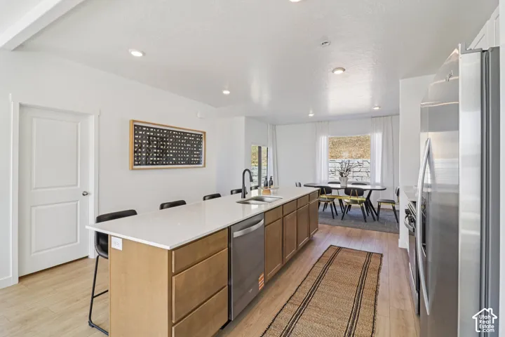 Kitchen island featuring light-finish cabinetry, quartz countertops, an undermount stainless steel sink with a matte black faucet, and stainless steel dishwasher