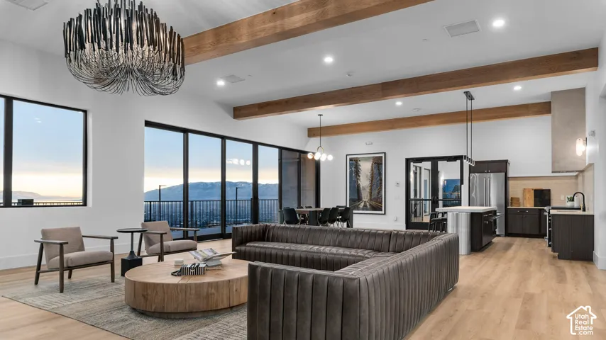 Vaulted ceilings accented by exposed wood-finish beams, expansive glass wall panels, custom pendant chandelier, wood-finish flooring, and integrated cabinetry