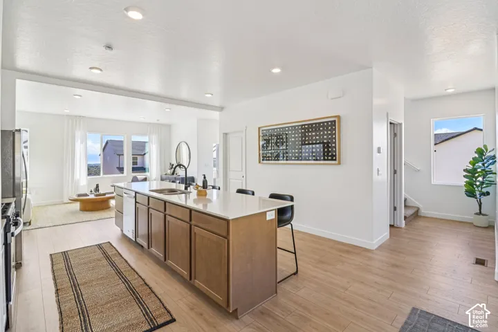 Kitchen island with a light-toned countertop, wood-finish cabinetry, stainless steel sink, recessed lighting, and wood-finish flooring