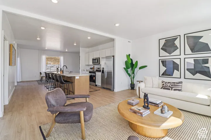 Open-concept kitchen featuring a waterfall-edge stone island, white shaker-style cabinetry, stainless steel appliances, and wood-finish flooring throughout