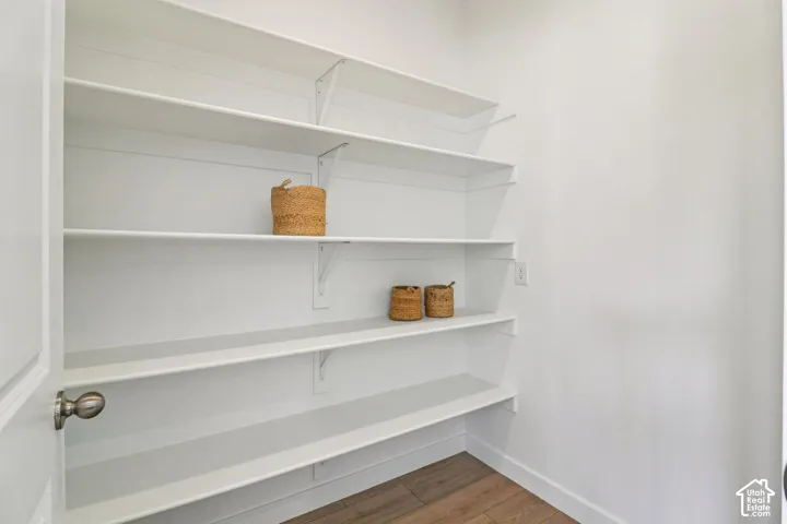 Storage space featuring multiple tiers of white shelving supported by metal brackets, complemented by wood-finish flooring