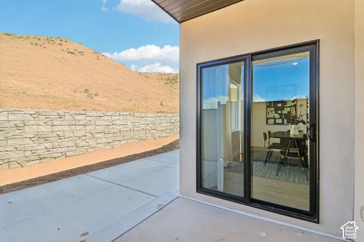 Covered concrete patio featuring a sliding glass door with a black frame and a stone-texture masonry retaining wall