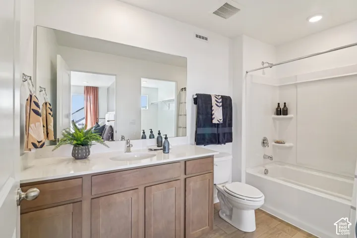Bathroom featuring wood-finish cabinetry, a white countertop with an integrated basin, a full-width mirror, and a tub-shower combination with built-in shelving