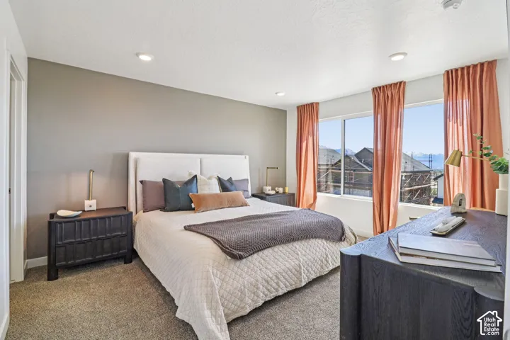 Neutral-toned bedroom featuring recessed lighting, carpeting, and large picture windows showcasing a mountain backdrop