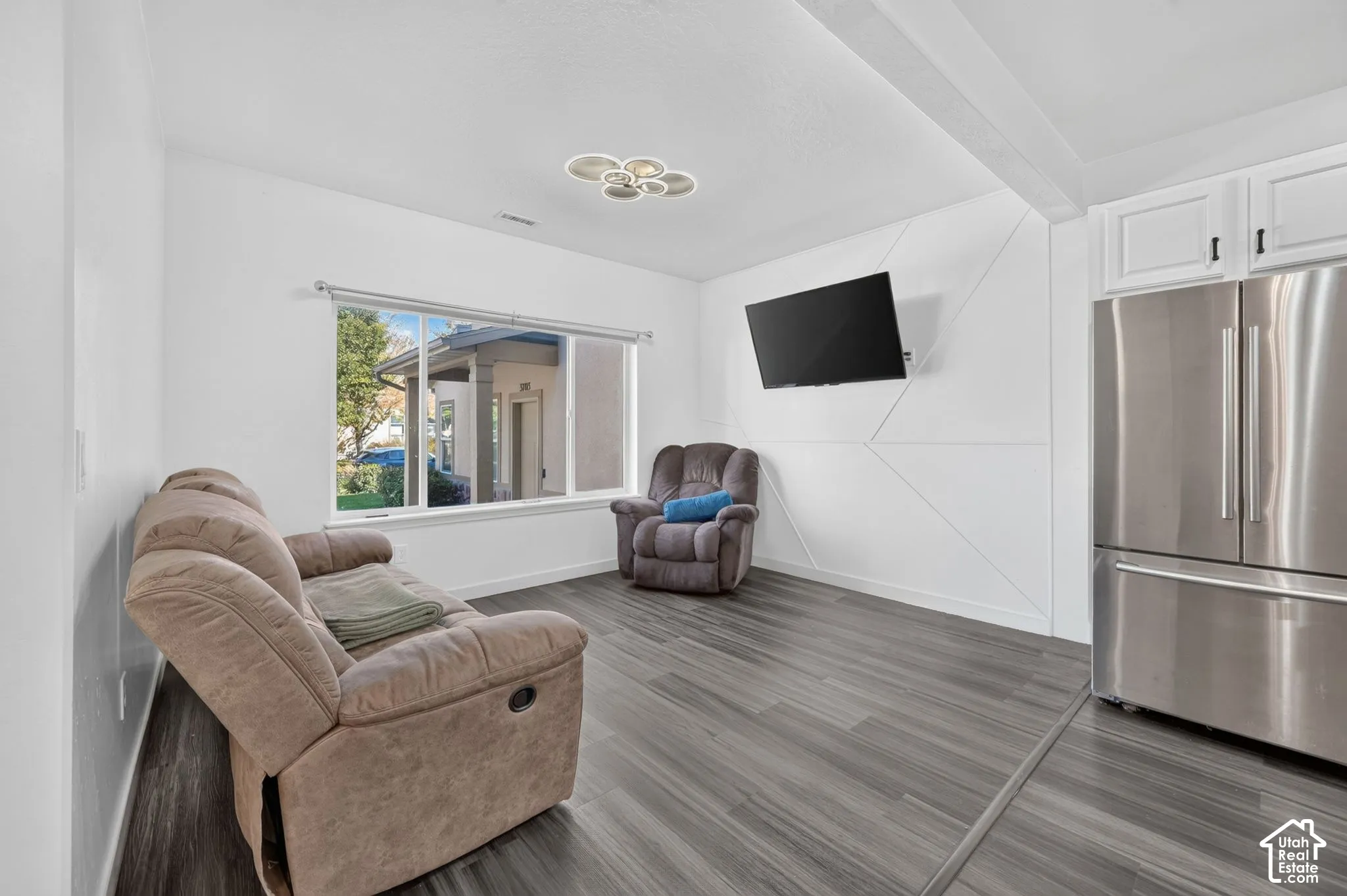 Wood-finish flooring, geometric wall paneling, stainless steel refrigerator, white cabinetry, and modern multi-ring ceiling fixture