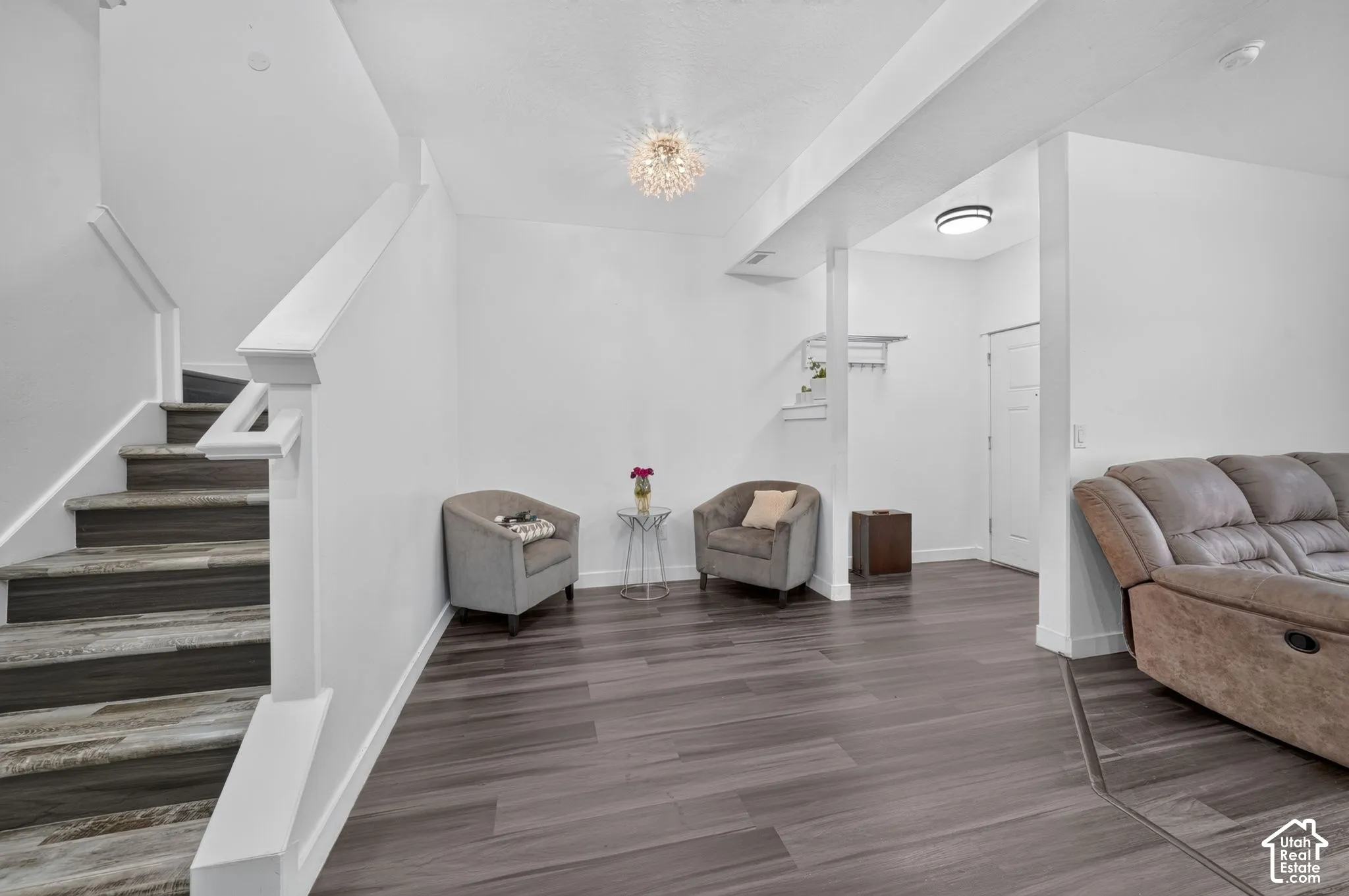 Wood-finish flooring, staircase with painted wood railings, crystal-style flush mount ceiling light, and built-in wall-mounted coat rack