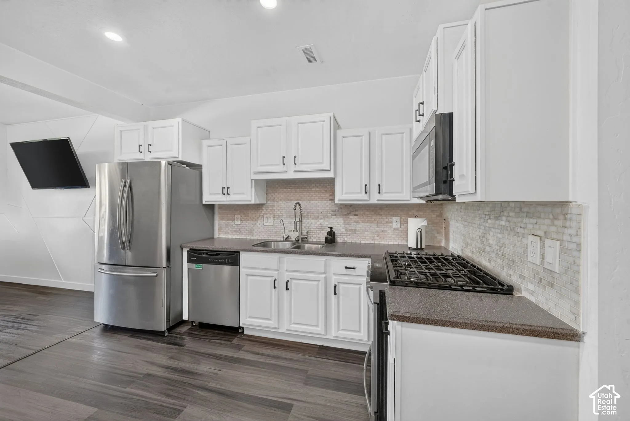 Kitchen featuring white cabinetry, stainless steel appliances, dark countertops, a stone-style mosaic backsplash, and wood-finish flooring