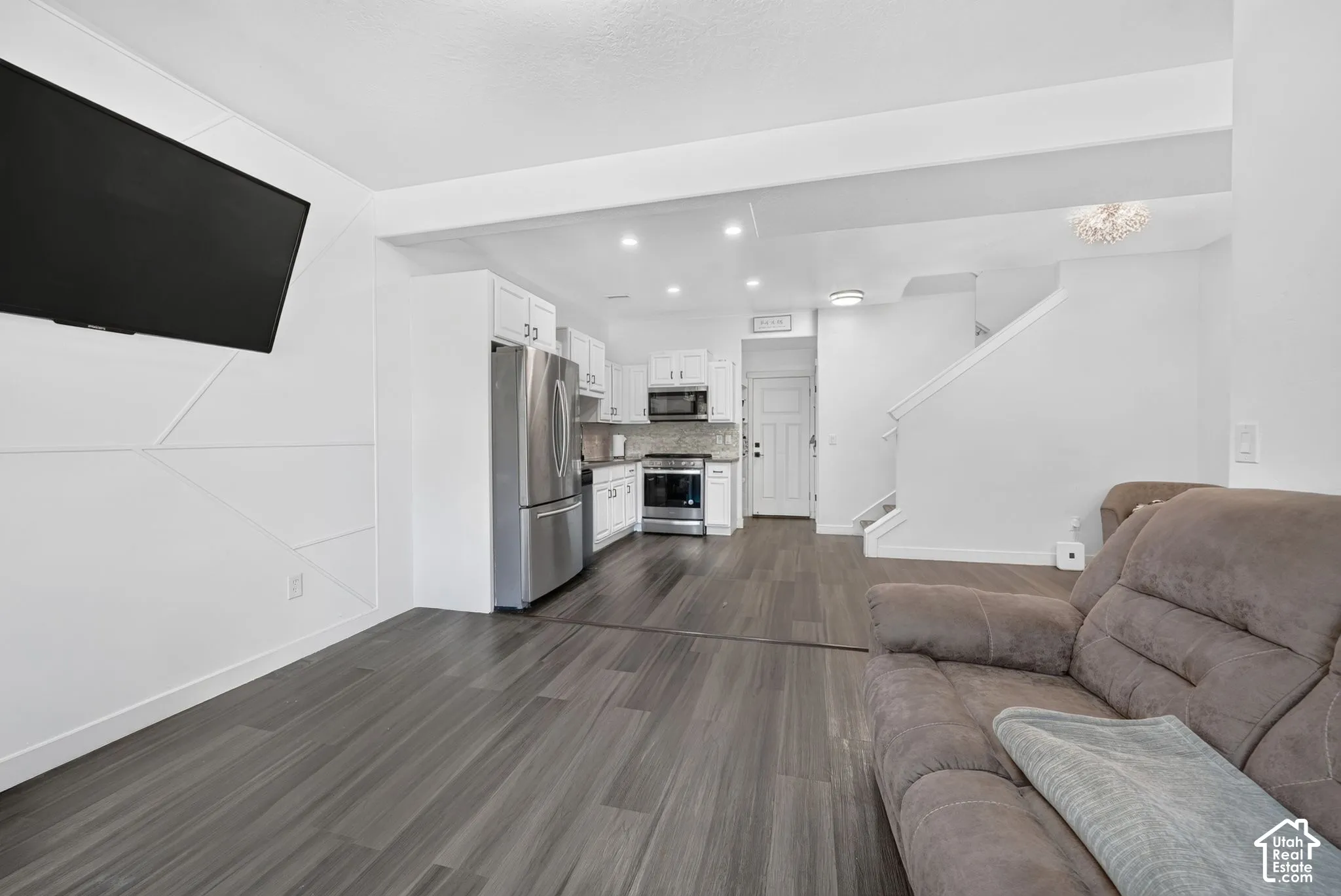 Open-concept interior featuring wood-finish flooring, a kitchen with white cabinetry, stainless steel appliances, and a geometric accent wall