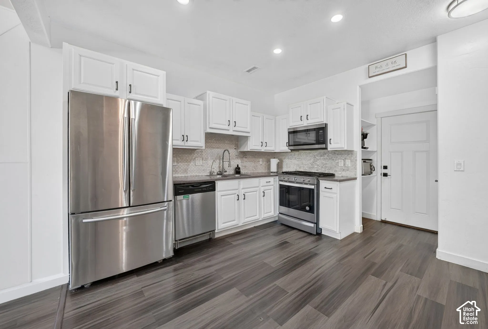 Kitchen featuring white shaker-style cabinetry, stainless steel appliances, patterned tile backsplash, solid-surface countertops, and wood-finish flooring