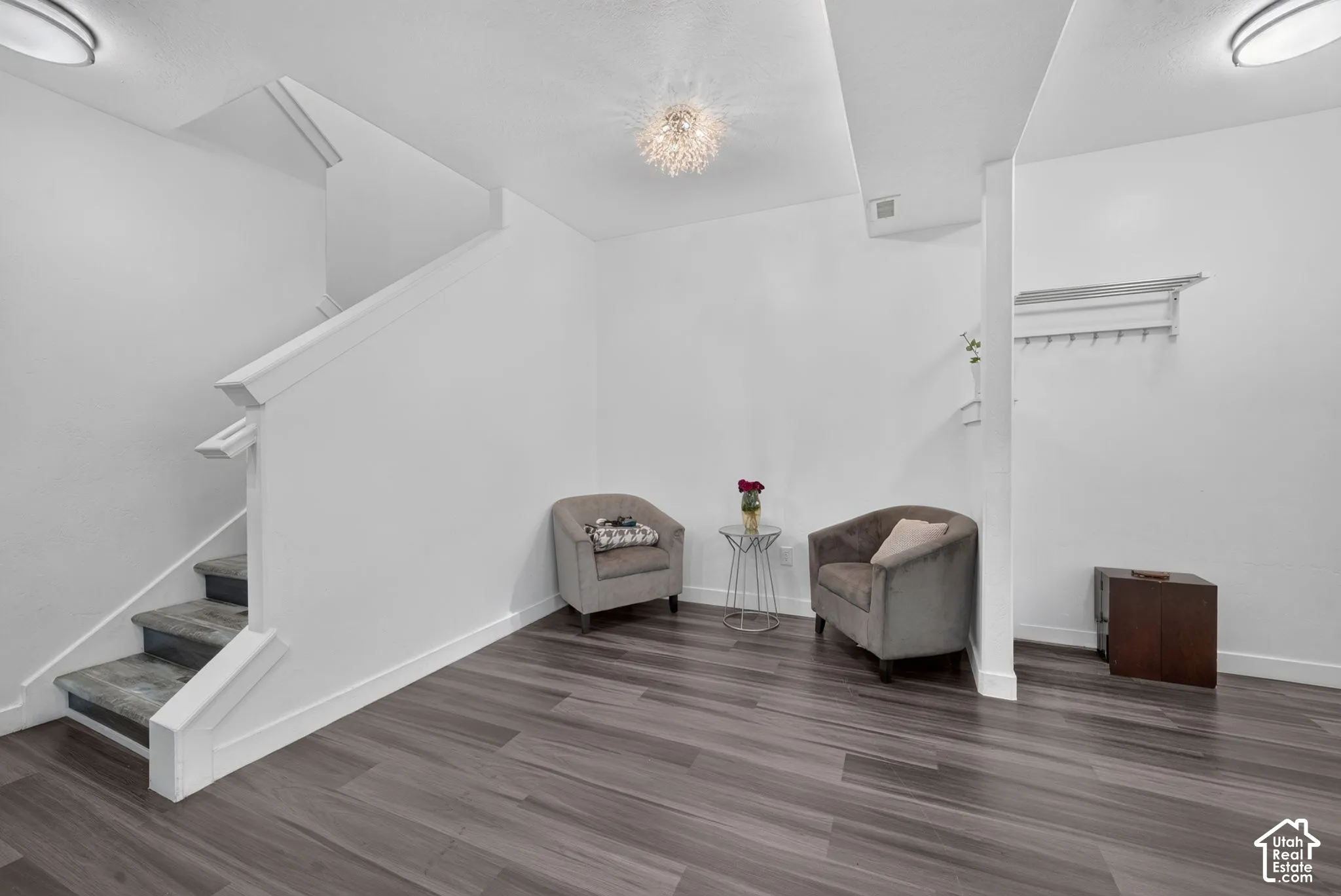 Interior area featuring wood-finish flooring, a staircase with a white balustrade, flush-mount ceiling lighting, and a wall-mounted coat rack