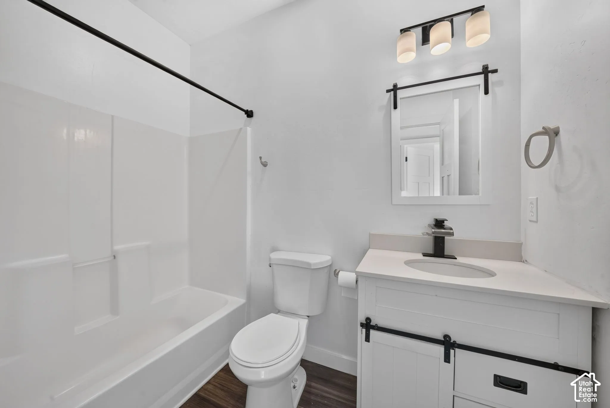 Bathroom featuring wood-finish flooring, white vanity with integrated basin and matte black hardware, barn-door style mirror frame, and a shower-tub combination with a matte black curtain rod