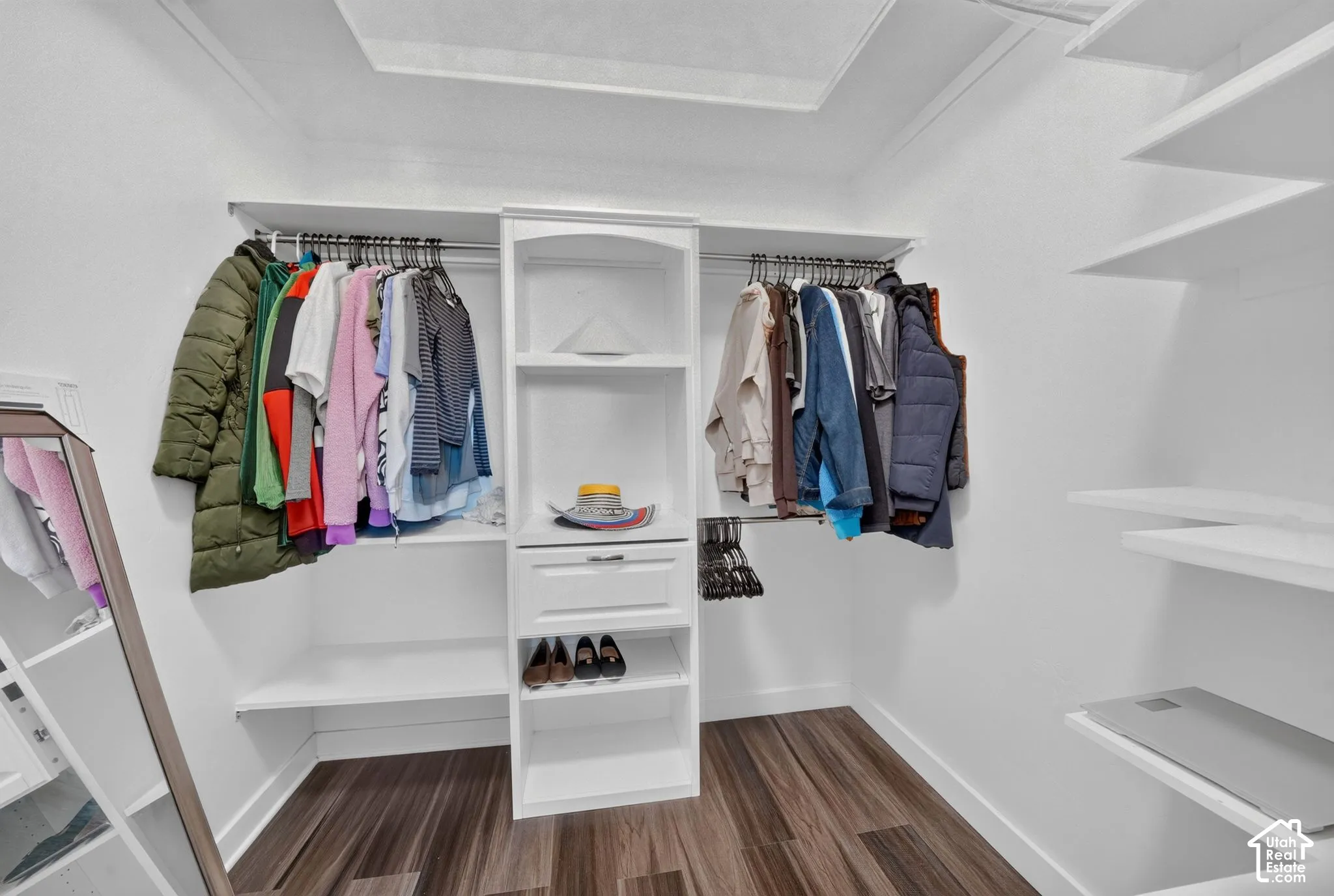 Walk-in closet featuring white built-in shelving, a central cabinetry unit with an integrated drawer, dual hanging rods, and wood-finish flooring