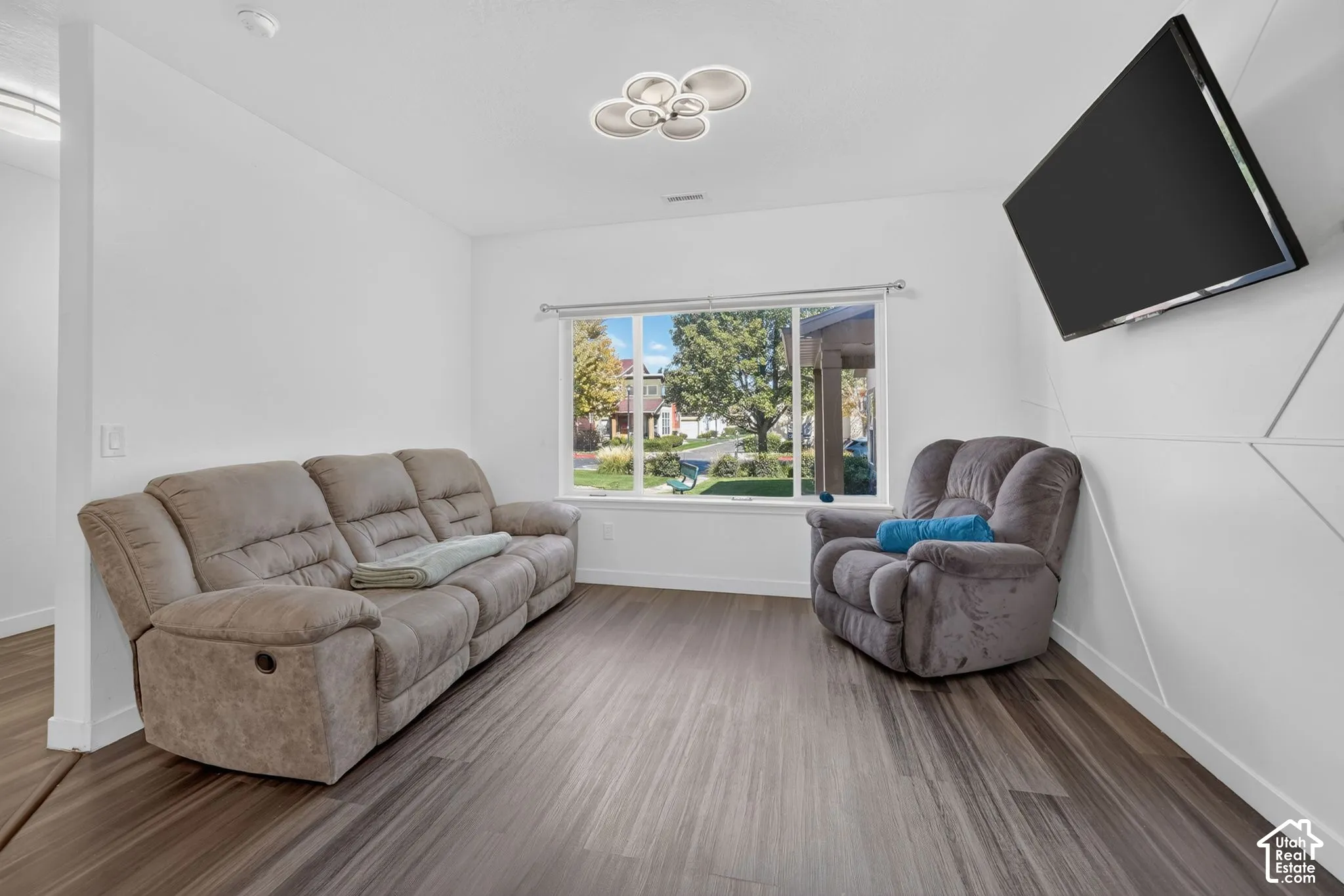 Wood-finish flooring, geometric wall paneling, multi-light flush-mount fixture, and expansive window with exterior greenery