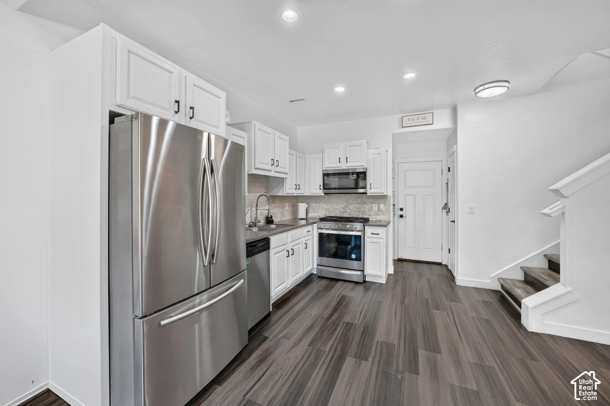 Kitchen featuring white shaker-style cabinetry, stone-finish countertops, stainless steel appliances, and wood-finish flooring