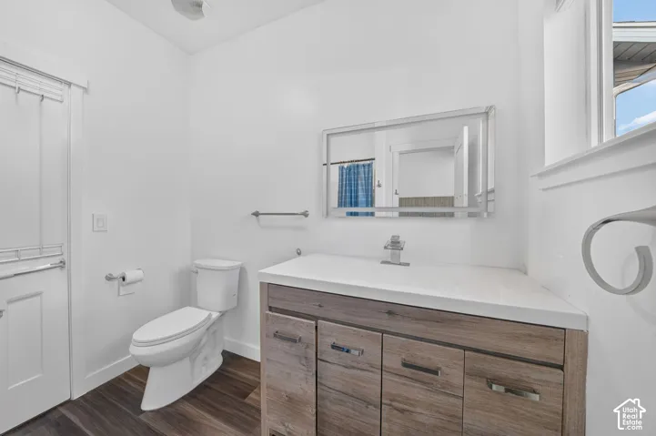 Vanity with wood-finish cabinetry, integrated countertop with rectangular basin, polished chrome faucet, rectangular framed mirror, and wood-finish flooring