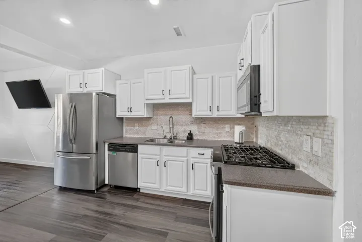 Kitchen featuring white cabinetry, stainless steel appliances, dark countertops, a stone-style mosaic backsplash, and wood-finish flooring