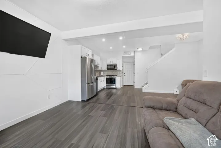 Open-concept interior featuring wood-finish flooring, a kitchen with white cabinetry, stainless steel appliances, and a geometric accent wall